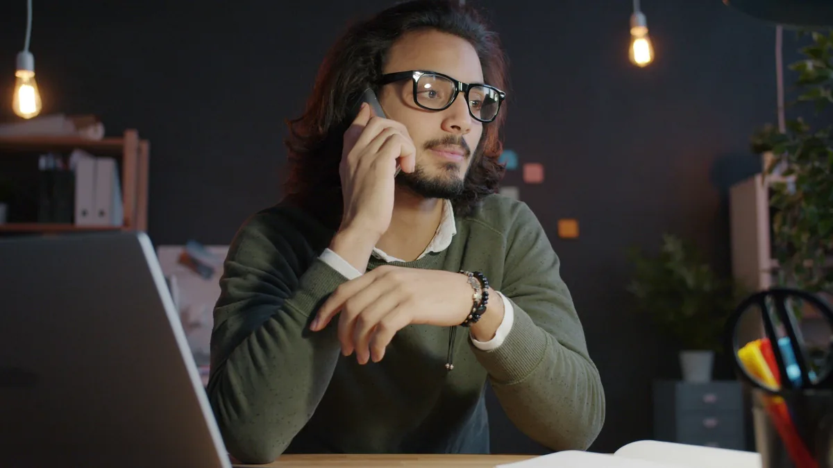Man in glasses taking a phone call at an office desk at night
